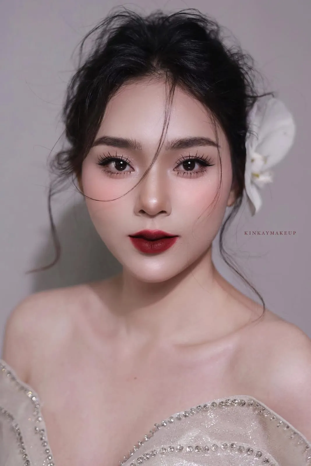 Cô dâu búi tóc thấp cài lan trắng, mắt nâu nhạt, môi đỏ trầm, KINKAY Sài Gòn