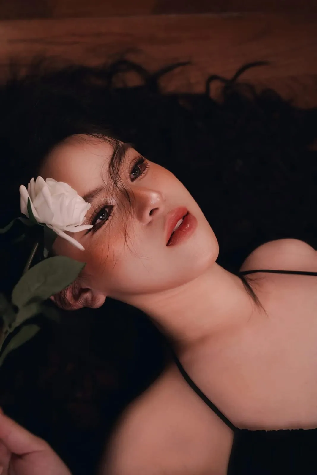 Nằm nghiêng cầm hoa hồng trắng che mắt, môi đỏ nâu, KINKAY Sài Gòn